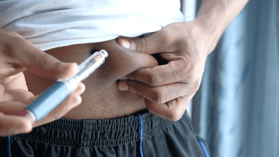 A person pinches the skin on their abdomen and prepares to inject medication with an insulin pen.