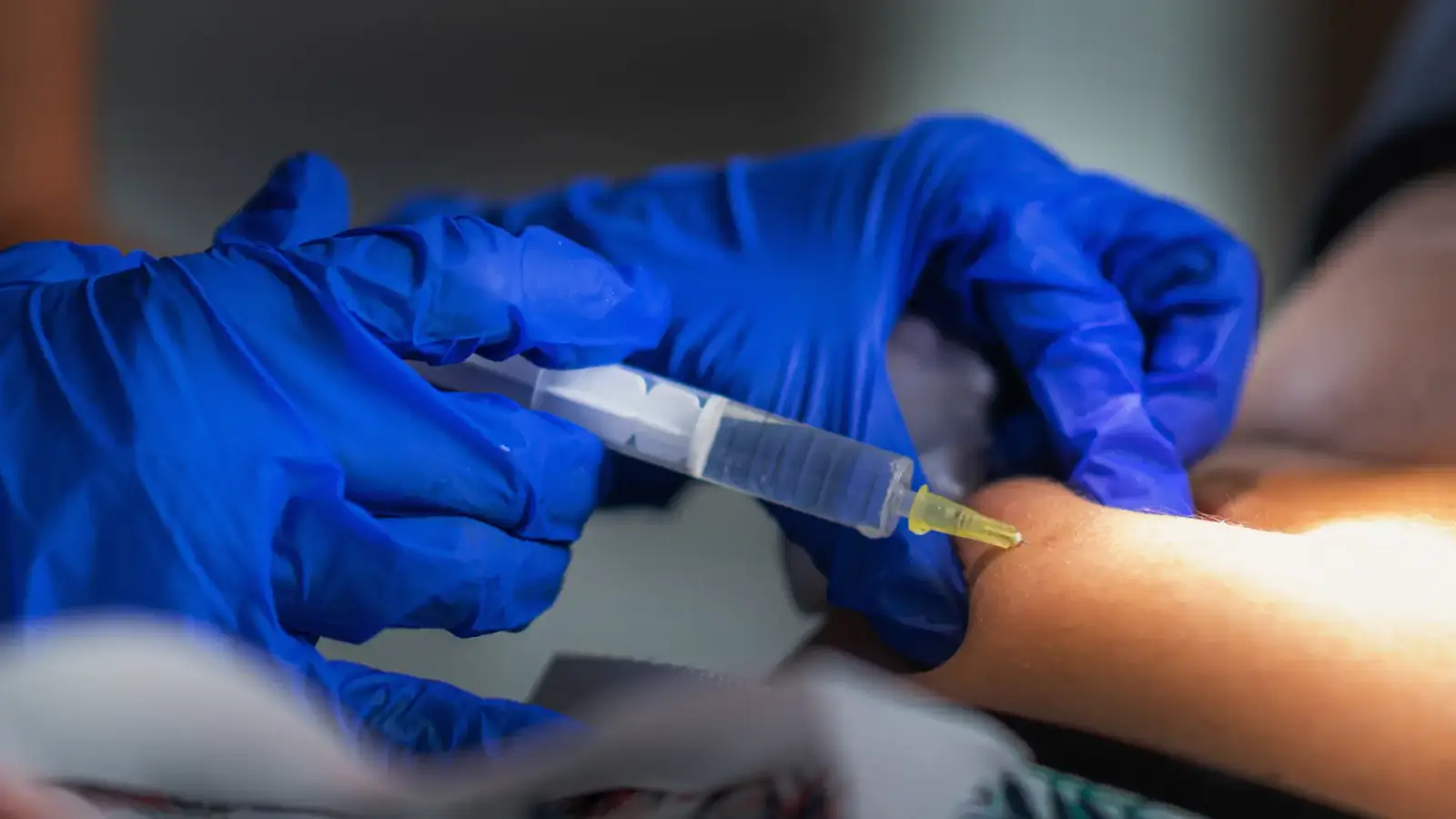 A close-up of gloved hands administering an injection with a syringe.