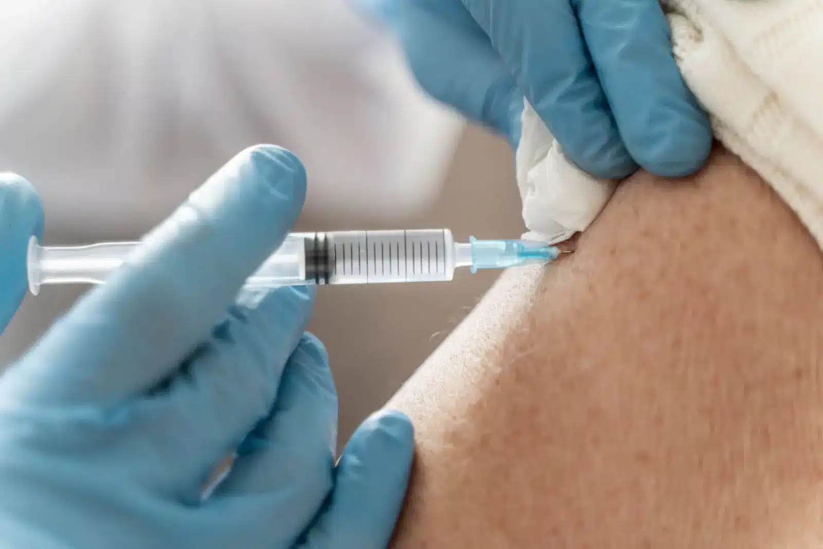 A close-up of gloved hands administering an injection with a syringe into a person's arm.