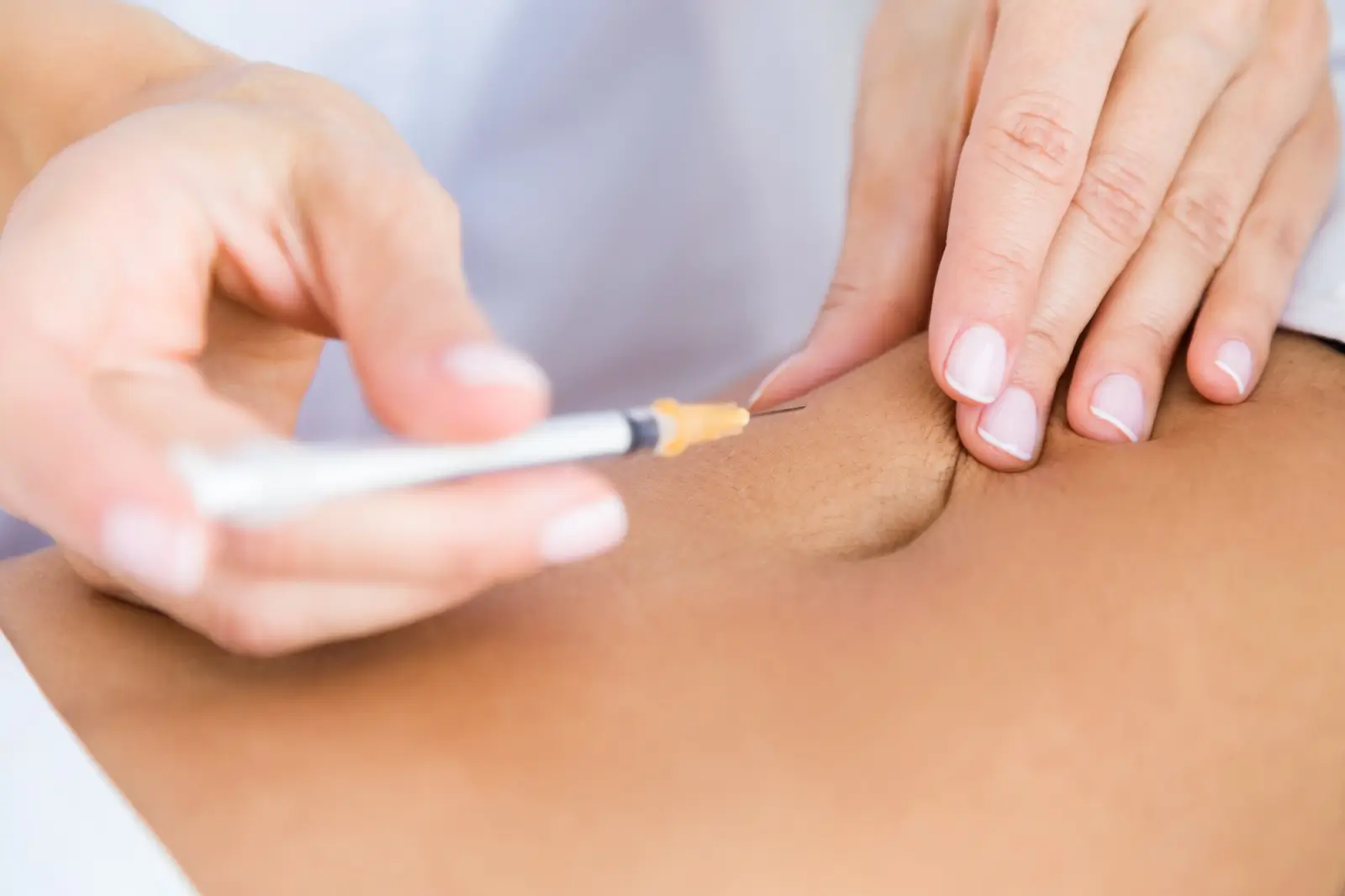 A close-up of hands administering an injection with a syringe into a person’s abdomen, suggesting a medical procedure or treatment.