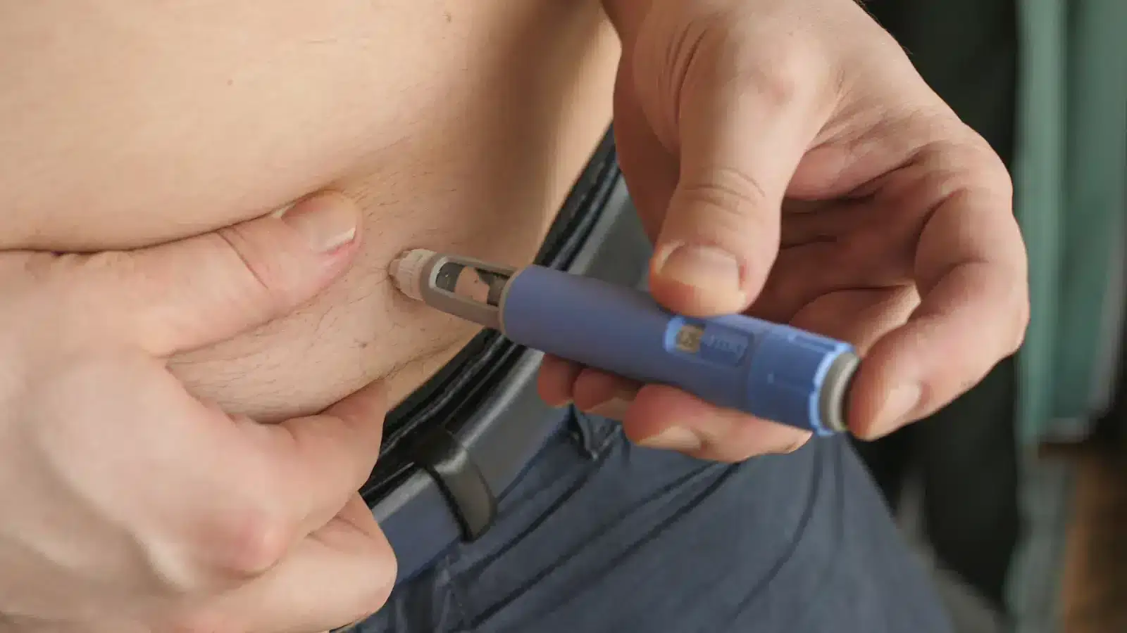 A person injects medication into their abdomen using an insulin pen, pinching their skin with one hand and holding the pen with the other.