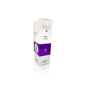 A white and purple box of STYLAGE® M BI-SOFT®, a cosmetic dermal filler product. The packaging features text and logos, showcasing a prominent purple band in the middle that indicates the product type. The box is photographed on a clean, white background.