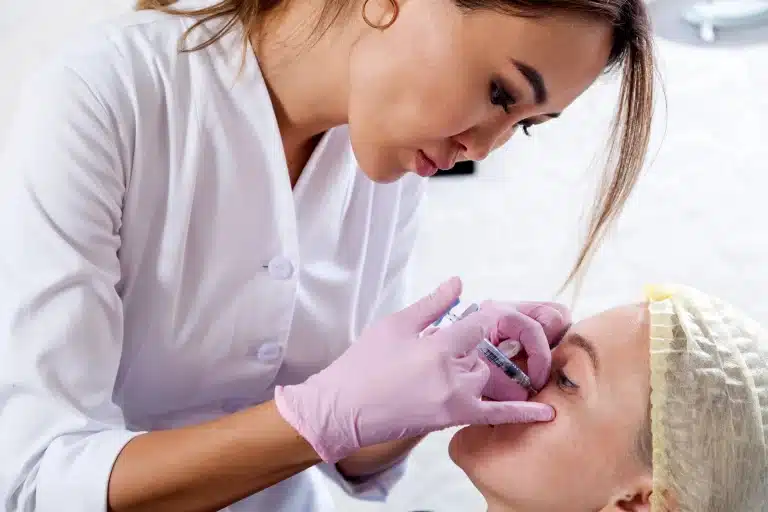 Medical professional providing beauty treatment to patient. Patient is relaxed, with eyes closed, while medical professional looks focused.