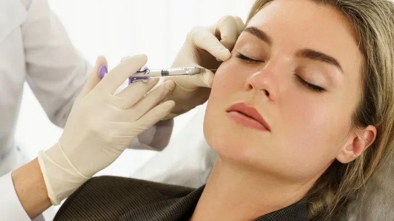 A woman with closed eyes is receiving a facial injection from a medical professional wearing gloves. She appears relaxed as the procedure is being conducted, focusing on her cheek area.