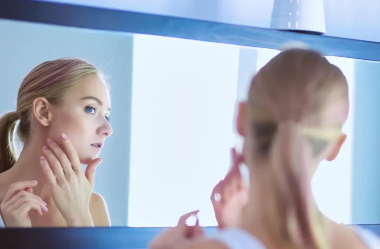 A woman checks her skin in the mirror following a dermal filler treatment.