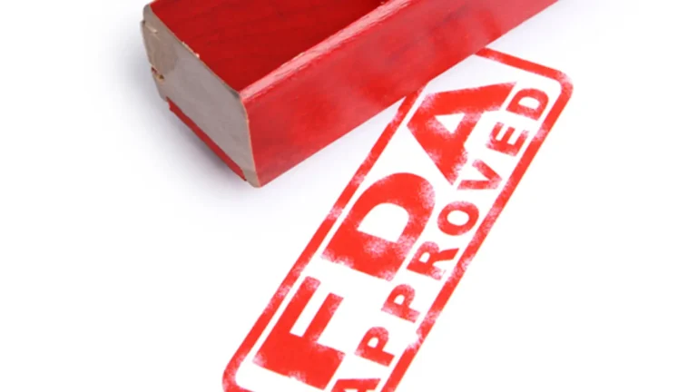 A red stamp with the text "FDA APPROVED" lying next to a wooden handle. The stamp is prominently displayed on a white background.