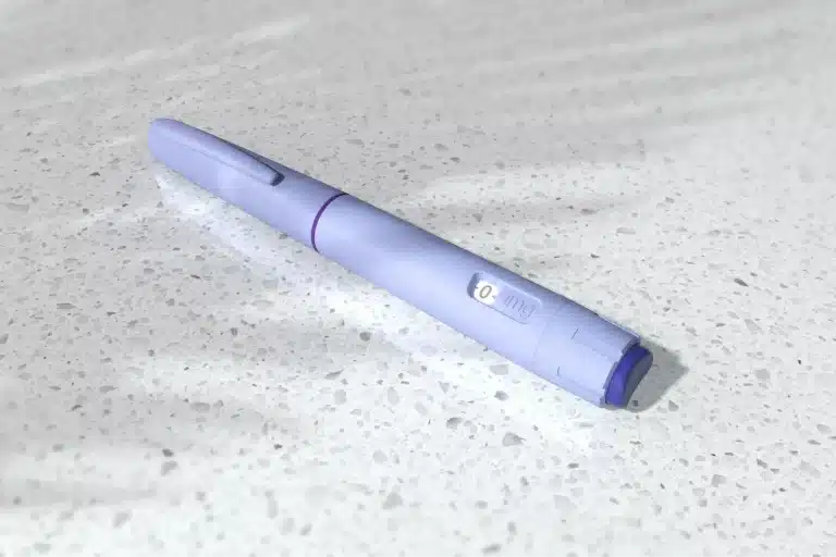 A lavender insulin pen injector with a clip lies on a speckled white countertop, casting a soft shadow with faint light streaks—prompting the question: does Saxenda need to be refrigerated?.