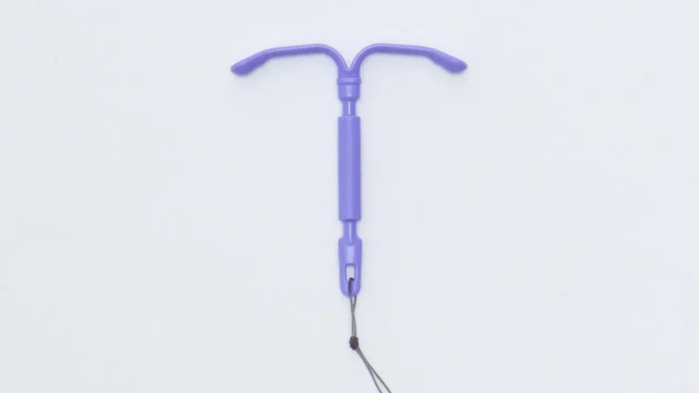 A purple intrauterine device (IUD) with two curved arms and attached strings is shown on a plain white background.