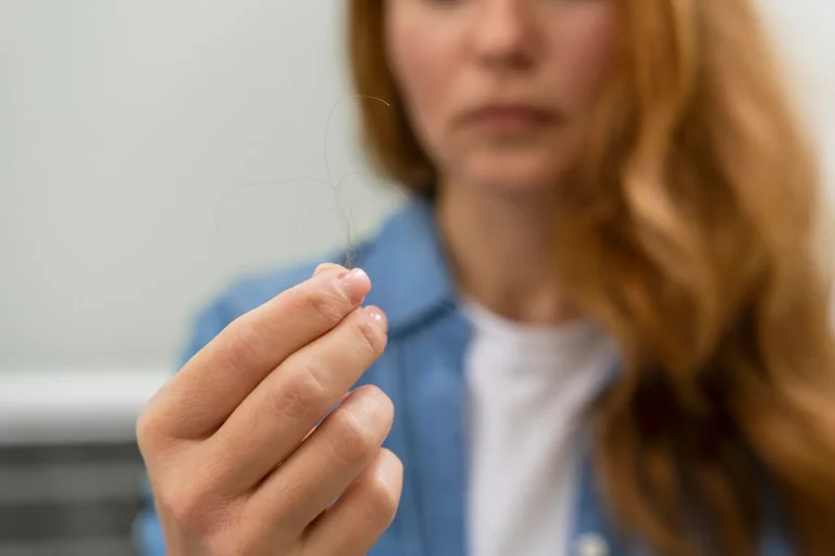 A woman with long red hair holds a few strands of hair in her hand, with her face out of focus in the background.