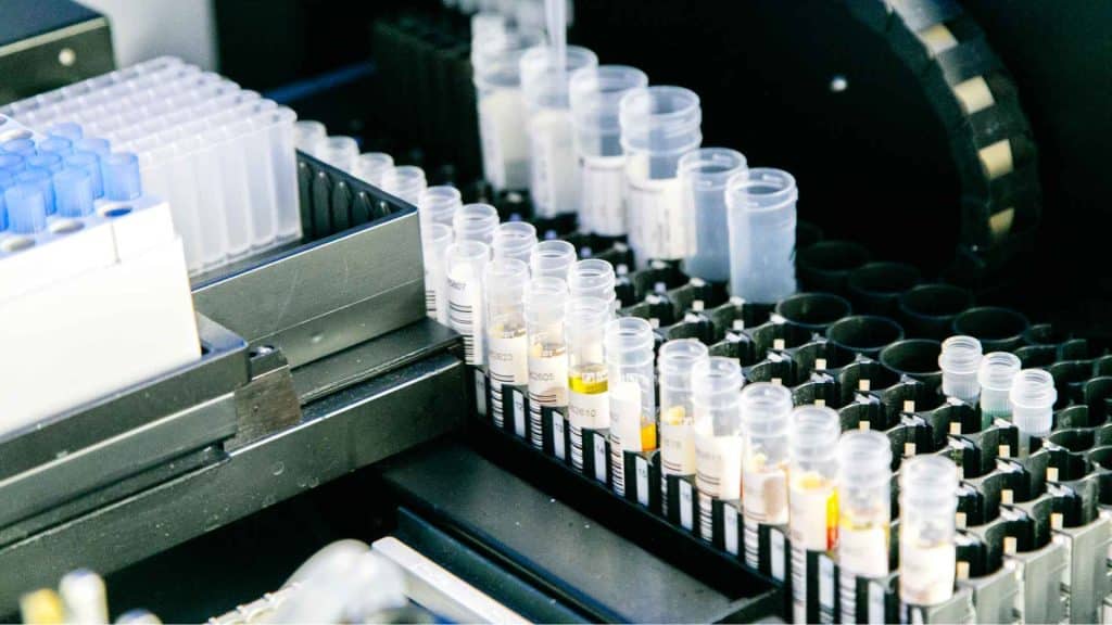 Rows of labeled test tubes filled with various liquids are organized in black trays inside a laboratory testing machine.