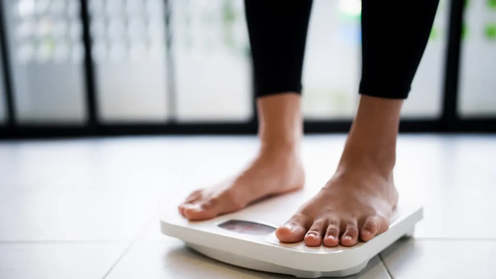 A person wearing black leggings standing on a digital bathroom scale.