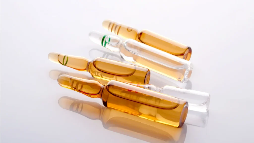 Four glass pharmaceutical ampoules, two containing amber liquid and two empty, arranged on a white surface.