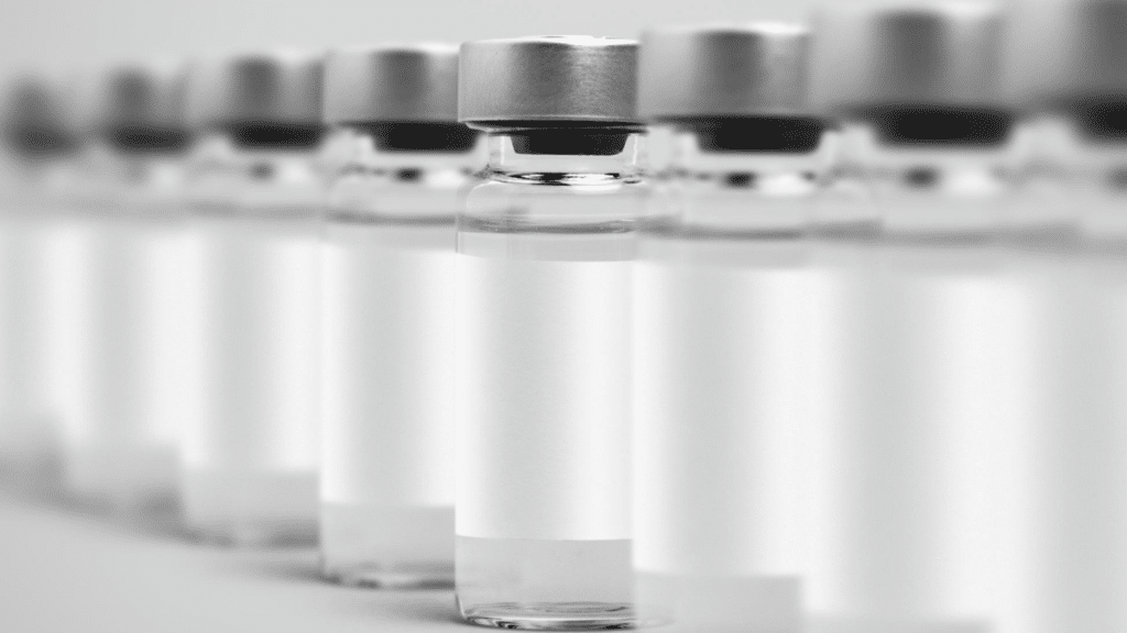 A row of clear glass medicine vials with metal caps and blank labels.