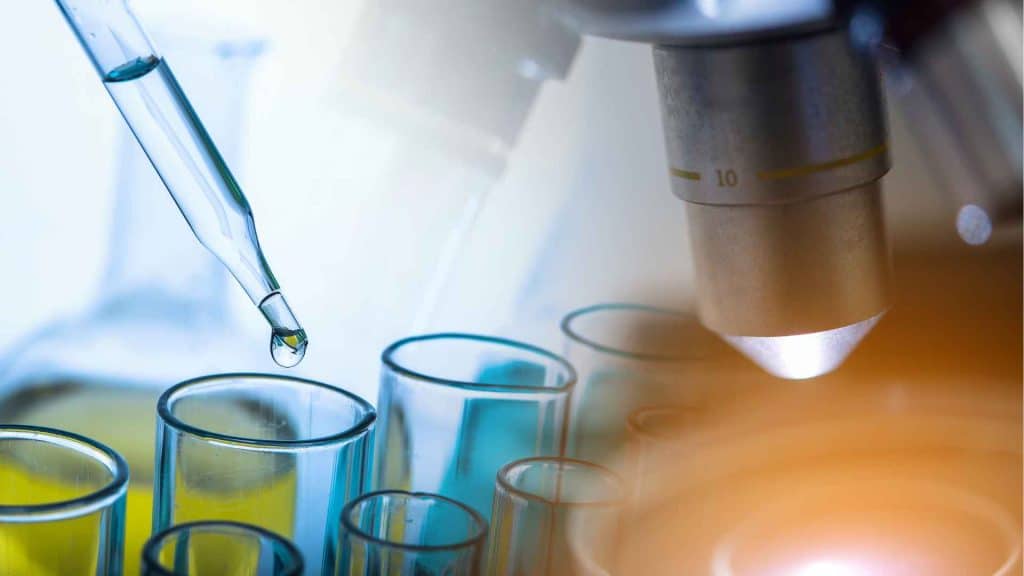 A dropper dispenses liquid into a test tube next to a microscope.